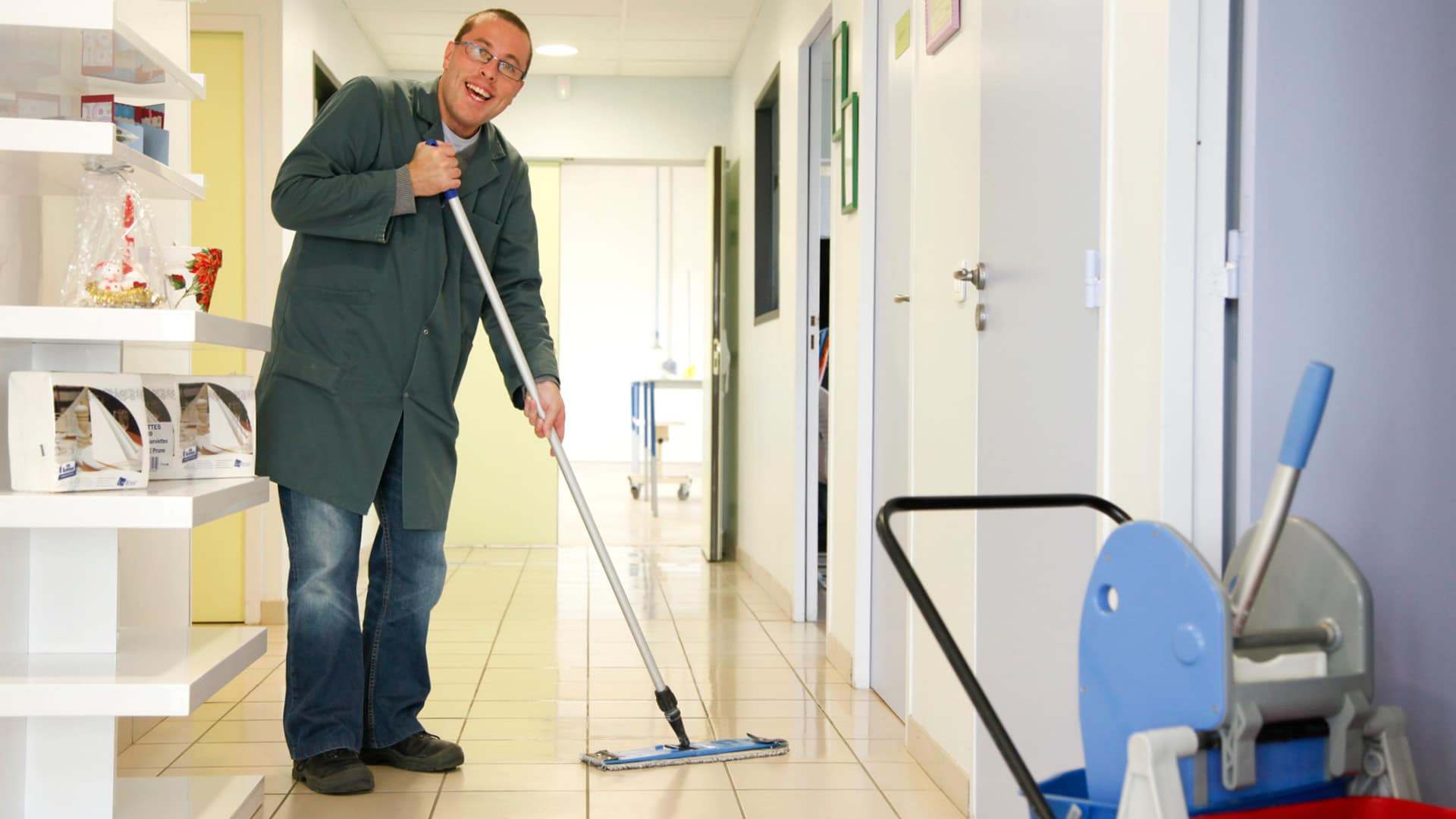 Employé très souriant qui passe la serpillière dans un couloir de bureau