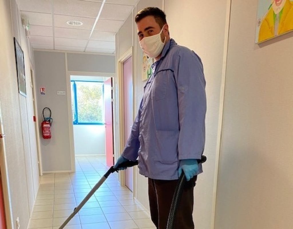 Employé en situation de handicap passant l'aspirateur dans un couloir